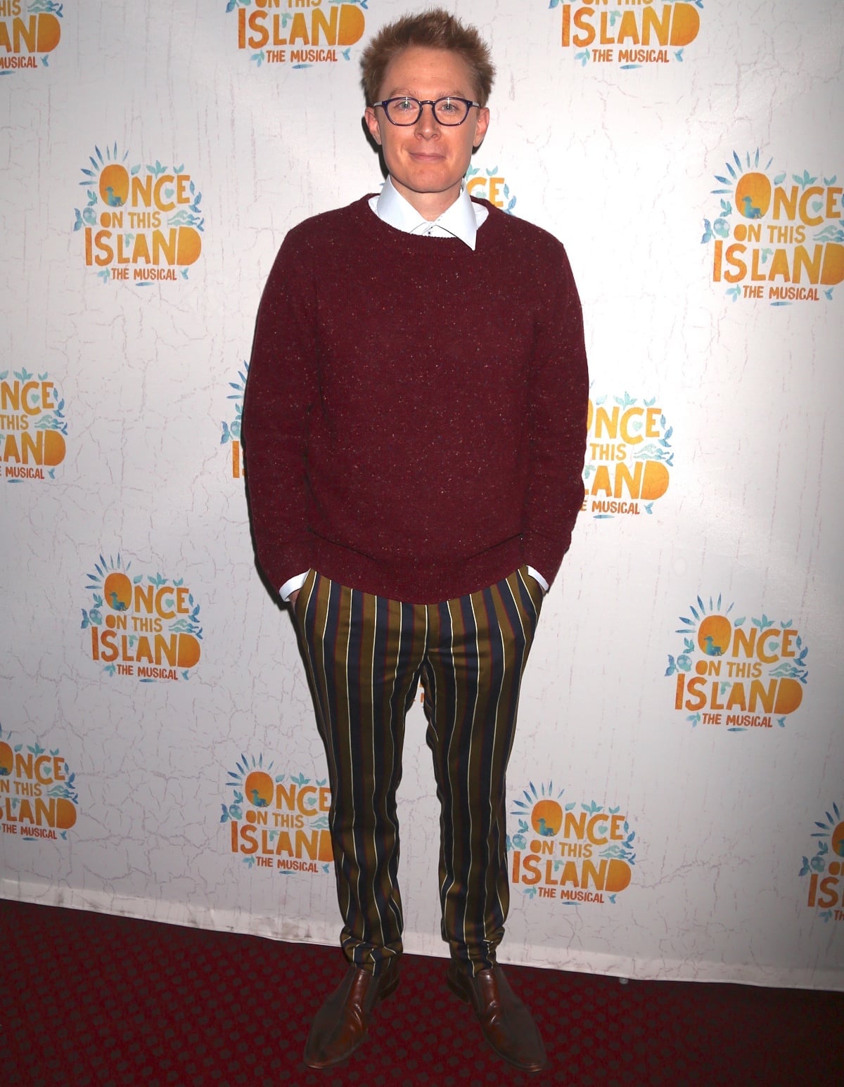 Clay Aiken adds a playful twist to classic style in a burgundy sweater, collared shirt, and bold striped trousers, grounded by sleek brown leather shoes at Once on This Island: The Musical