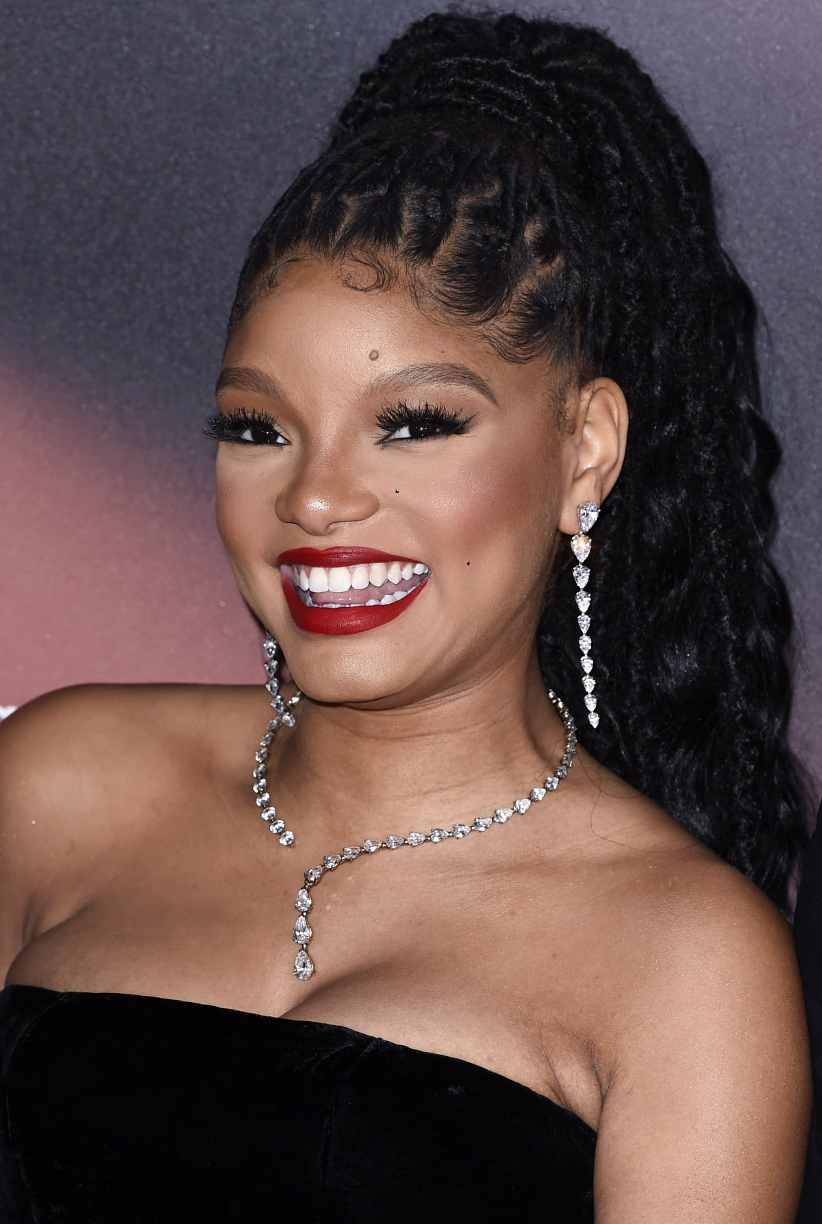 Halle Bailey’s beauty look consisted of long braids secured in a high ponytail, a bold red lip, and Anabela Chan jewelry