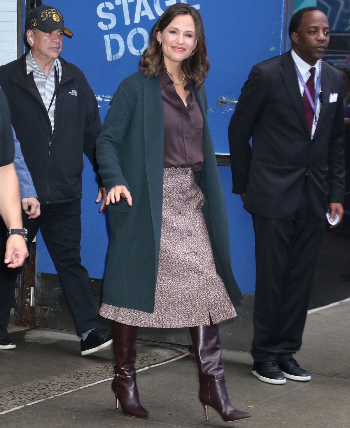 Jennifer Garner embraced polished autumn layering in a deep teal coat, satin brown blouse, and textured boucle skirt, finishing the seasonal palette with sleek chocolate-brown knee-high leather boots featuring sharp pointed toes and slim stiletto heels