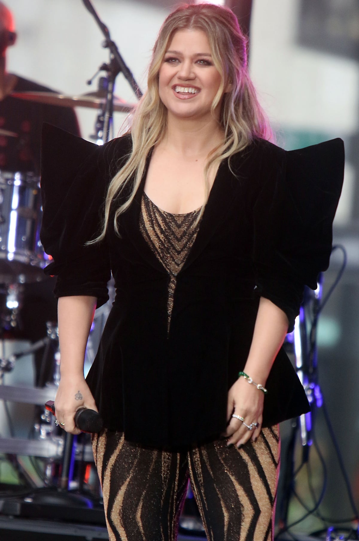 Kelly Clarkson commands the stage in a structured black velvet jacket layered over a glittering tiger-striped bodysuit, blending bold glamour with rockstar edge during her live performance