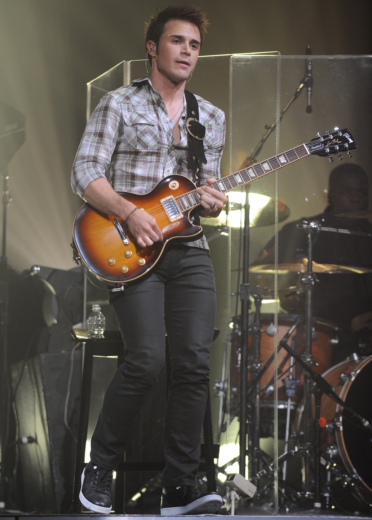 Kris Allen rocks the stage in a plaid button-up shirt, skinny black jeans, and black high-top sneakers, delivering a laid-back yet polished performance look
