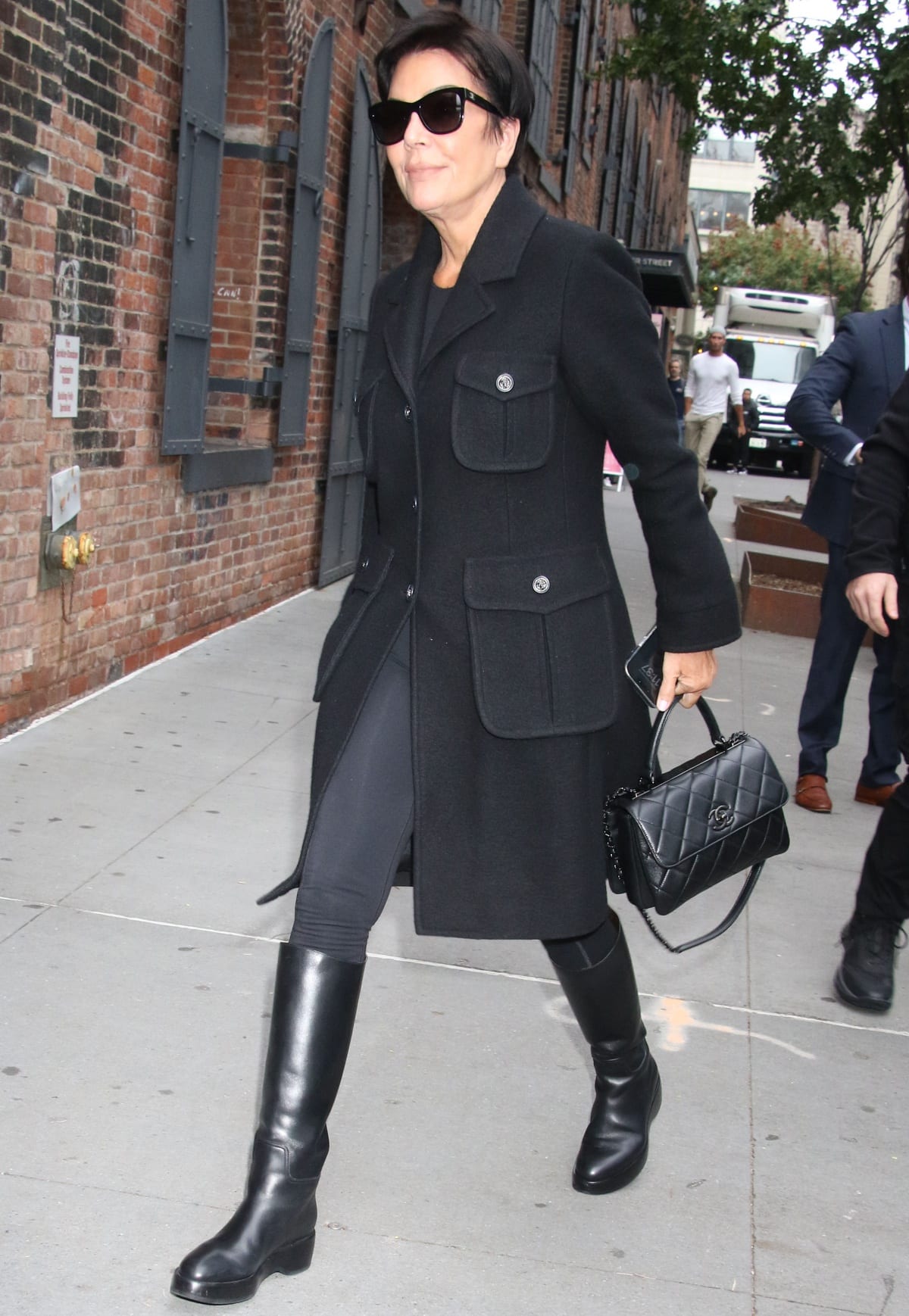 “Kris Jenner, elegantly clad in a monochromatic black outfit, paired a tailored coat and leggings with sleek knee-high leather boots and a quilted Chanel bag for a timeless street-style moment