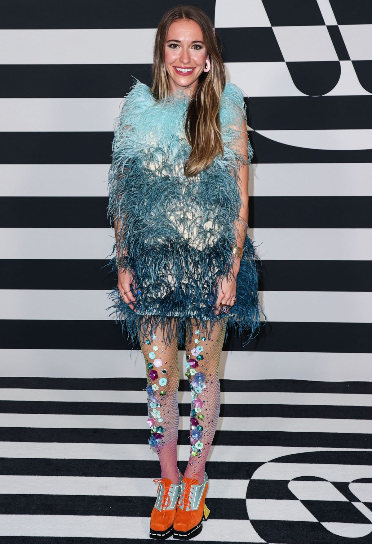 Lauren Daigle embraces a bold, eclectic style in a blue feathered mini dress, embellished mesh tights, and bright orange platform heels
