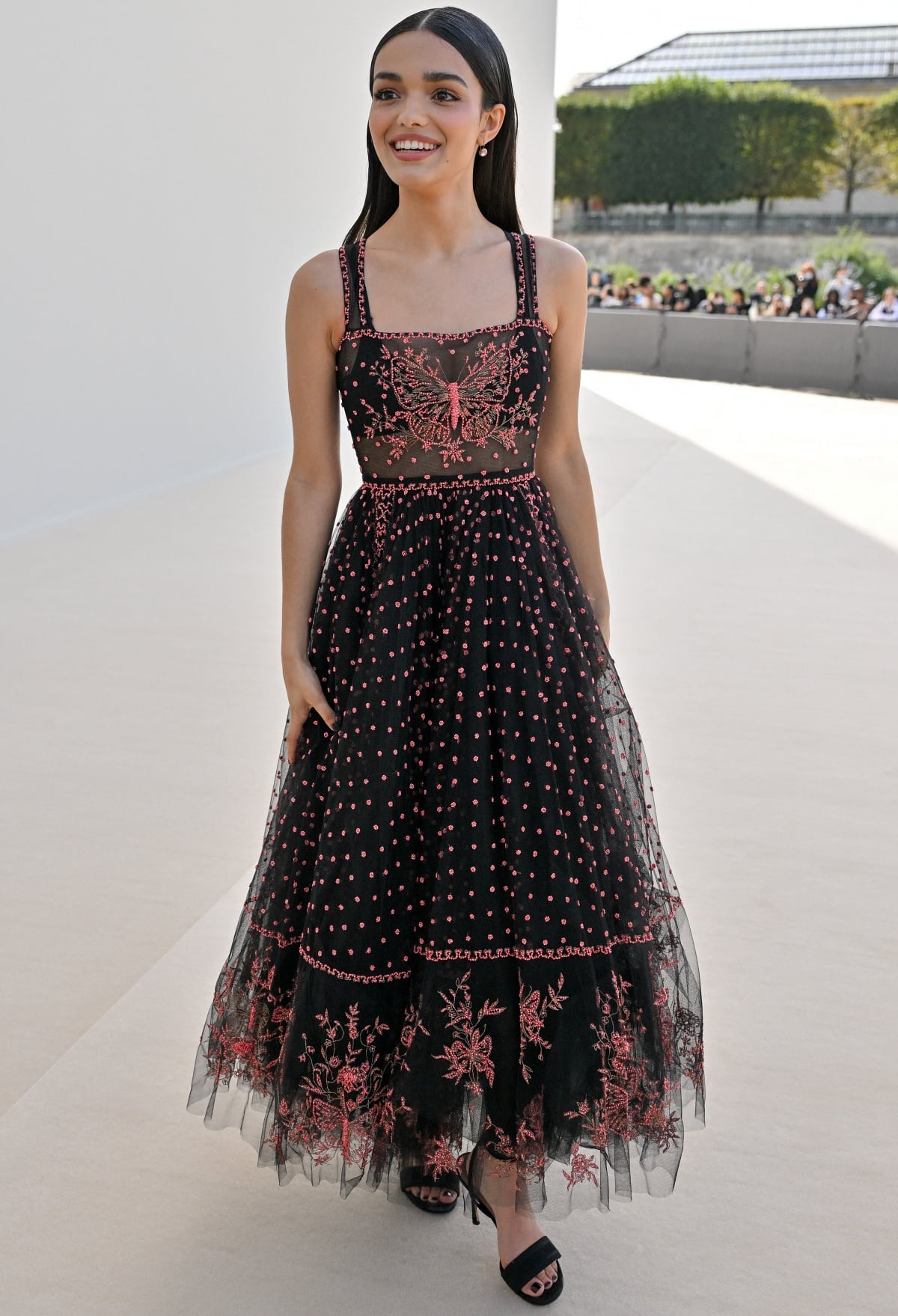 Rachel Zegler radiates effortless charm in a black-and-pink butterfly-embroidered Dior gown paired with the house’s Dway heeled sandals, whose sleek straps and slim silhouette add a refined lift to her petite 5′2″ frame