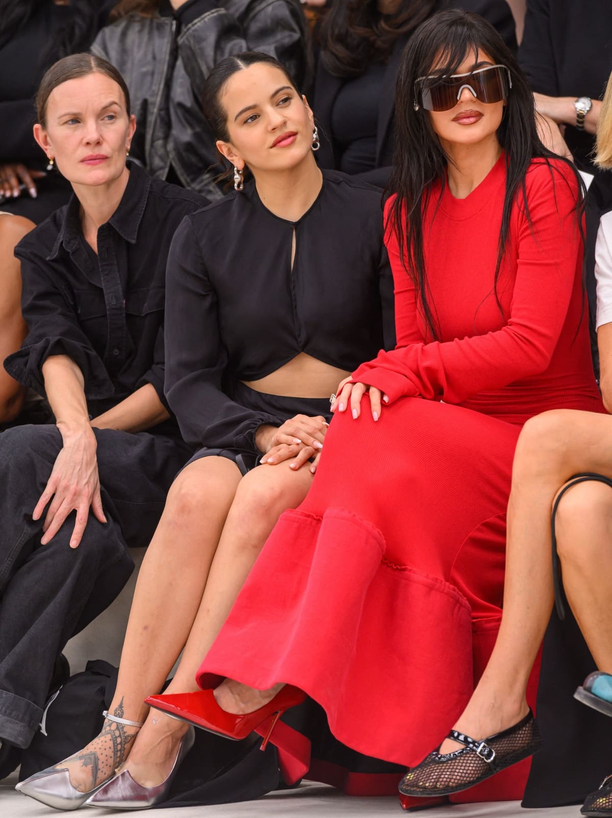 Rosalía, in silver strappy heels paired with a cut-out black dress, sat alongside Kylie Jenner, who showcased her scarlet pointed-toe pumps beneath a fiery red gown, as the two friends watched the Acne Studios Spring/Summer 2024 runway show from the front row