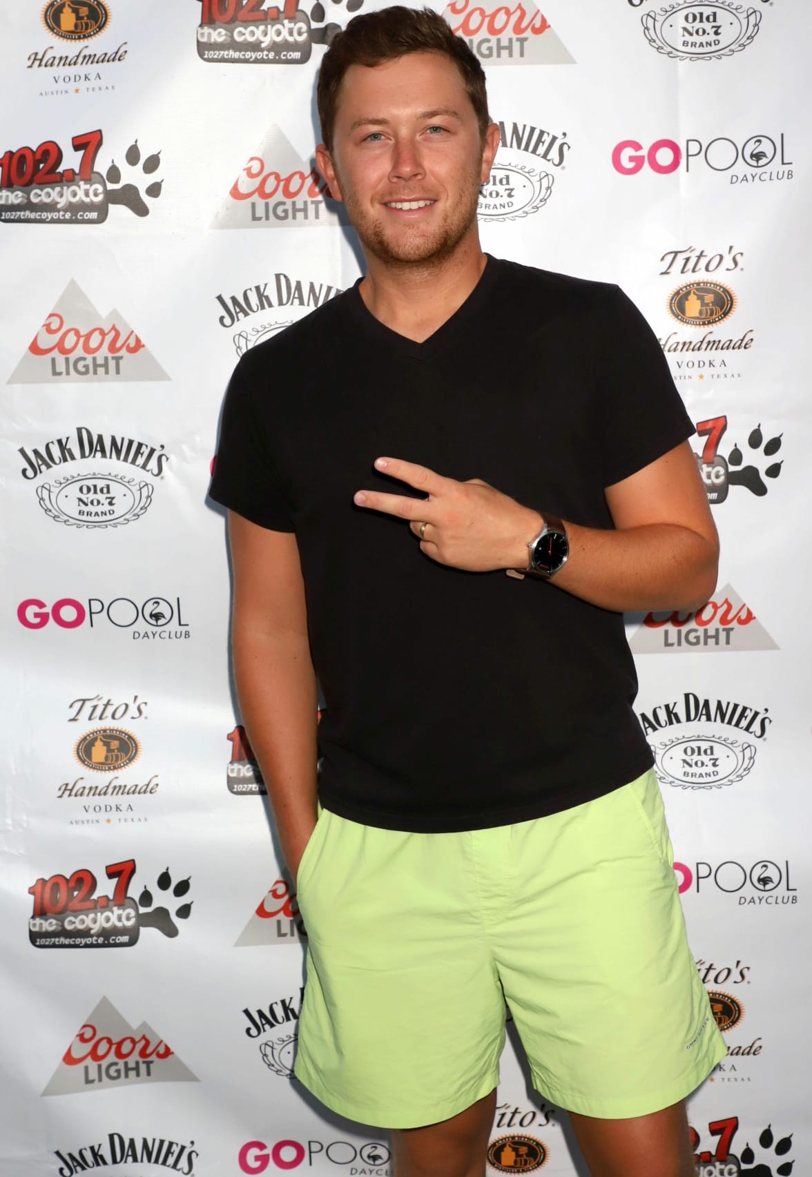 Scotty McCreery keeps it casual and cool in a black V-neck tee and neon green shorts, flashing a peace sign at a summer event hosted by 102.7 The Coyote and GO Pool Dayclub