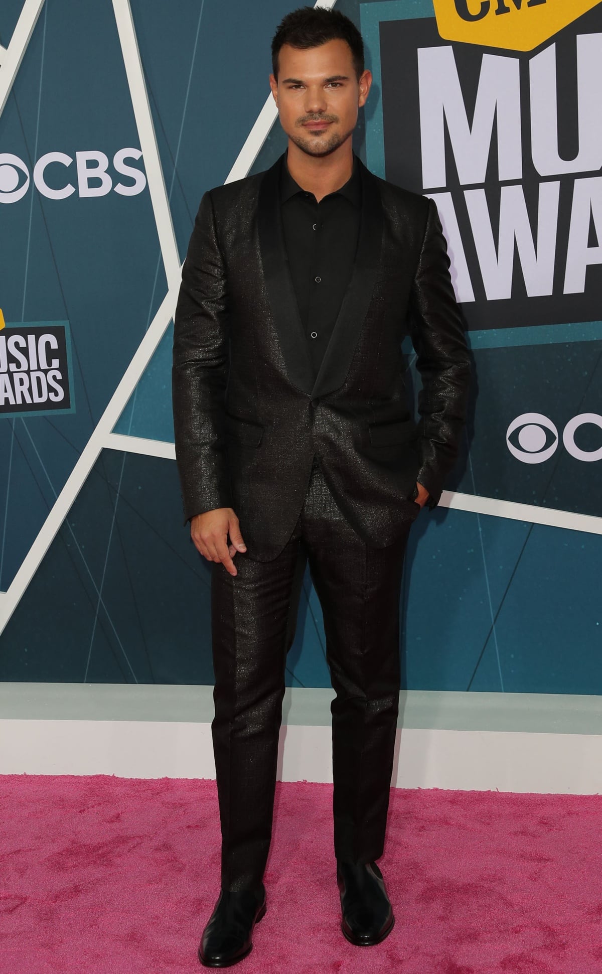 Taylor Lautner brought suave sophistication to the 2022 CMT Music Awards in a sleek, subtly shimmering black suit paired with classic black dress shoes, proving less is more on the pink carpet