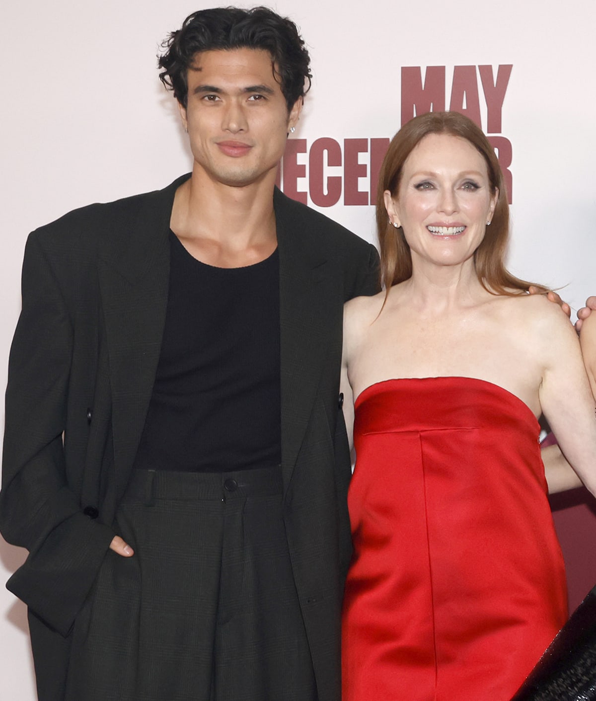 Julianne Moore glows in her strapless red Prada gown as she poses alongside Charles Melton, who keeps it effortlessly cool in a relaxed-fit black suit and matching crewneck