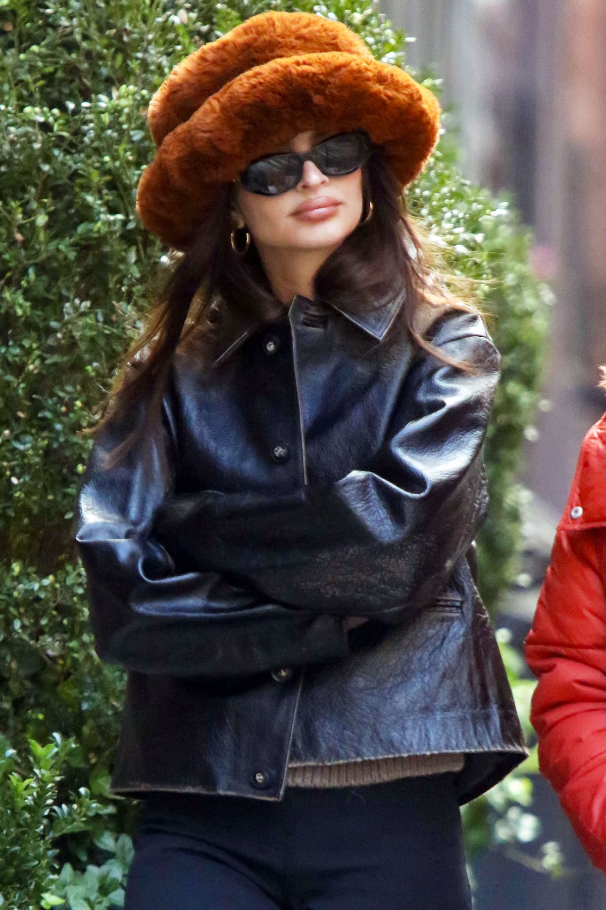 Emily Ratajkowski accessorizes her laid-back NoHo look with gold hoop earrings, slim black Fendi sunglasses, and soft nude makeup, complementing the retro feel of her oversized faux-fur bucket hat and leather jacket