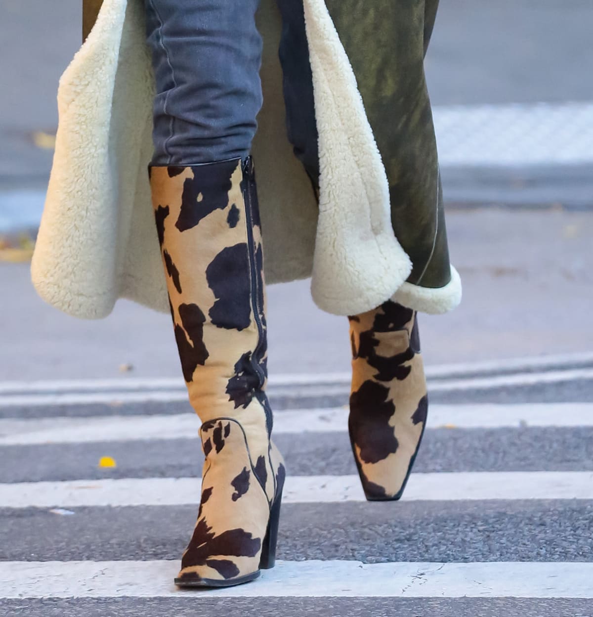 Emily Ratajkowski spotlights Fendi’s striking cow-print knee-high boots, pairing the statement calf-hair style with a vintage-inspired shearling-lined leather coat for a standout winter street-style moment