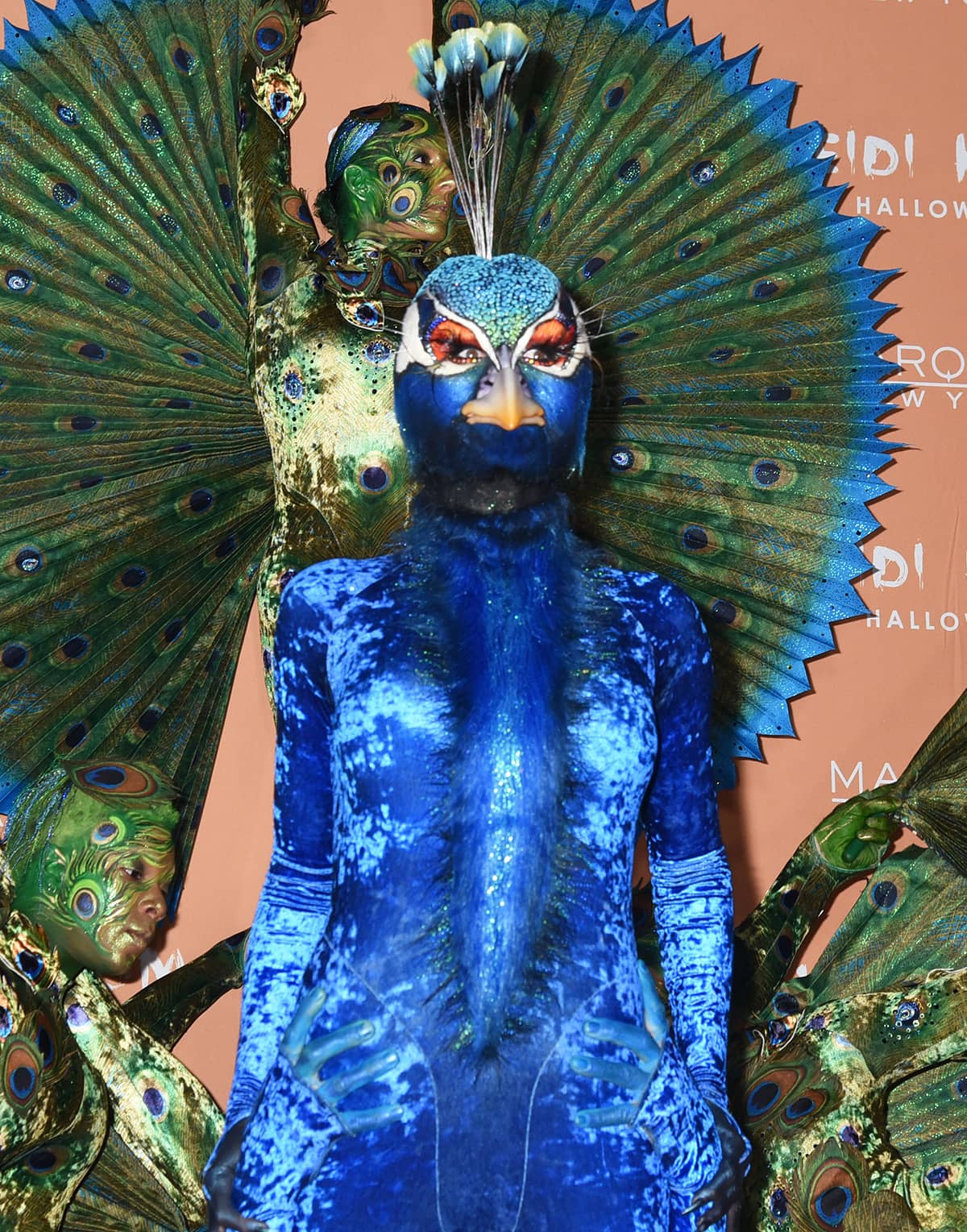 Heidi Klum showcases her stunning transformation in a feather-textured cobalt bodysuit and intricate beak prosthetic, complete with a sparkling blue headpiece and vibrant eye makeup