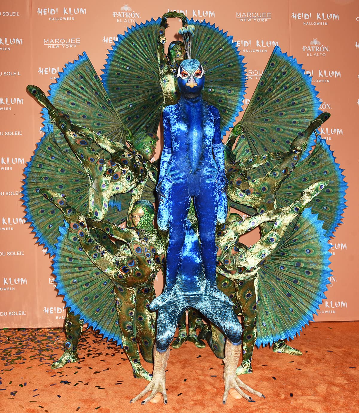 Heidi Klum completes her jaw-dropping peacock transformation with sculpted claw-like feet over nude heels, striking a commanding pose among Cirque du Soleil dancers at her 2023 Halloween party