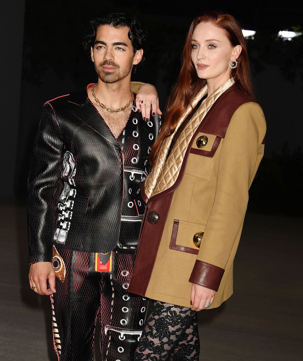 Joe Jonas and Sophie Turner make a bold fashion statement in coordinated Louis Vuitton ensembles at the 2nd Annual Academy Museum Gala on October 16, 2022, with Joe in a futuristic black grommeted suit and Sophie in a tan and burgundy coat layered over lace tights