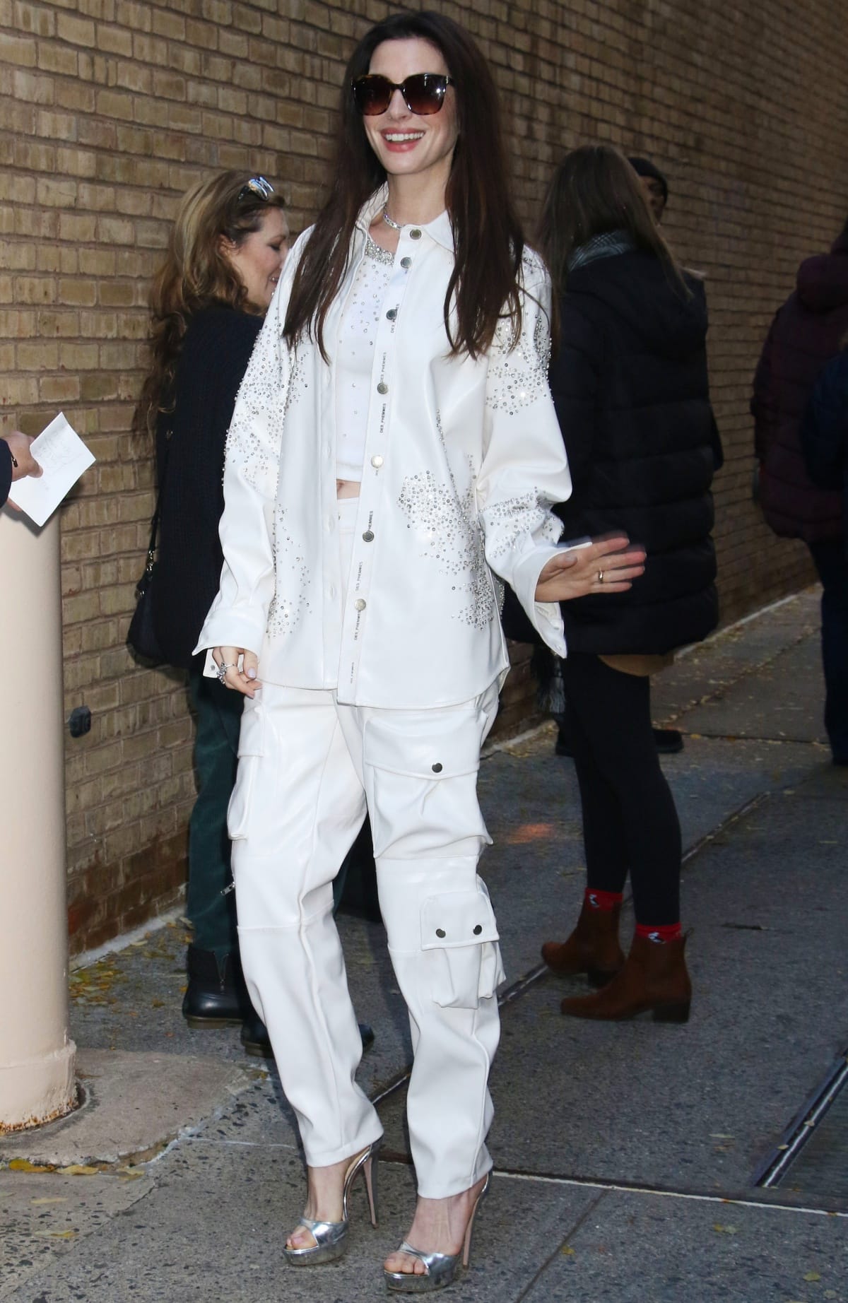 Anne Hathaway paired embellished white utility separates with towering metallic silver platform sandals while arriving at the Live with Kelly and Mark studios in New York City on November 27, 2023, balancing relaxed cargo silhouettes with polished high-shine glamour