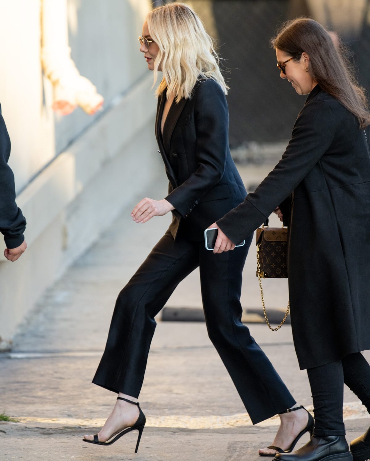 Emma Stone cuts a sleek figure in a black Louis Vuitton power suit, finishing the look with minimalist black ankle-strap stiletto sandals that add a sharp, leg-lengthening edge