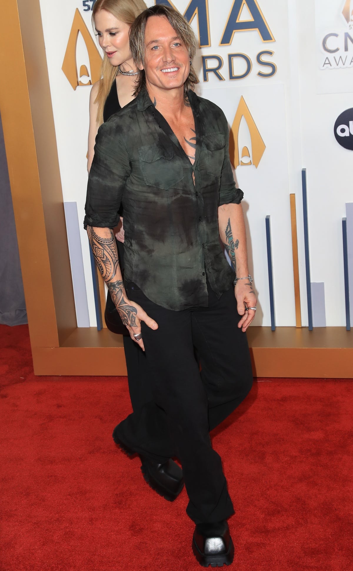 Keith Urban rocks a relaxed all-black outfit, pairing wide-leg trousers with chunky black Balenciaga lug-soled boots that add an edgy, casual contrast to Nicole Kidman’s glamorous gown