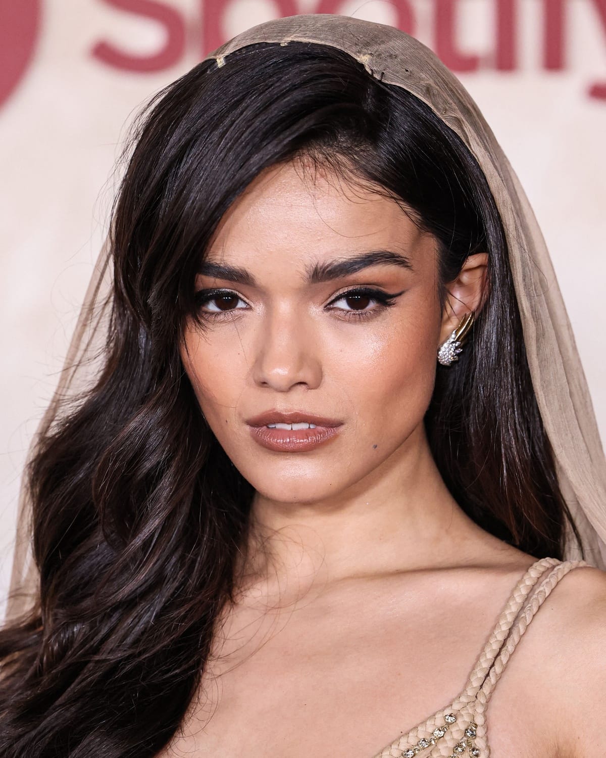 Rachel Zegler’s beauty look consisted of brunette waves, light bronze eye makeup, black winged liner, a nude-colored glossy lip, and Jean Schlumberger Flame silver earrings by Tiffany Co.