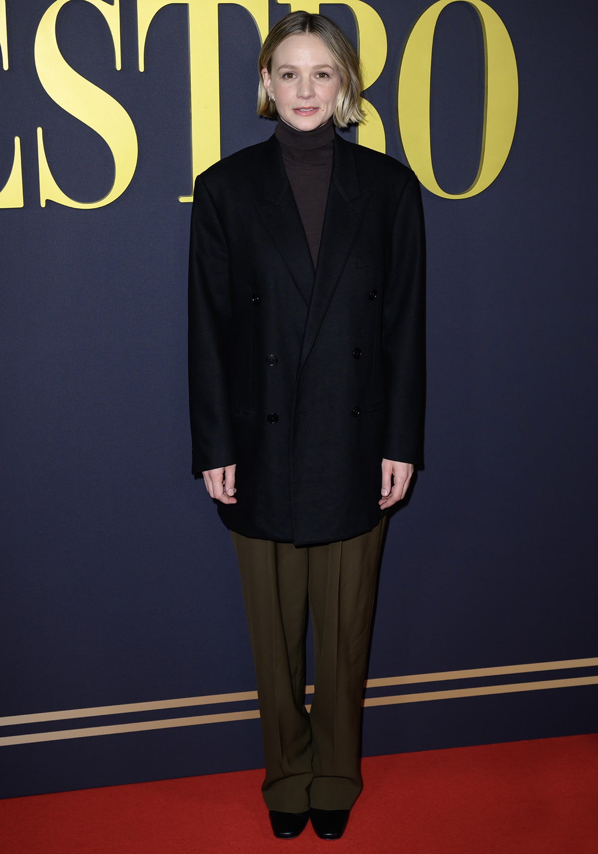 Carey Mulligan keeps it understated in a black oversized blazer, brown turtleneck, wide-leg olive trousers, and square-toed black shoes