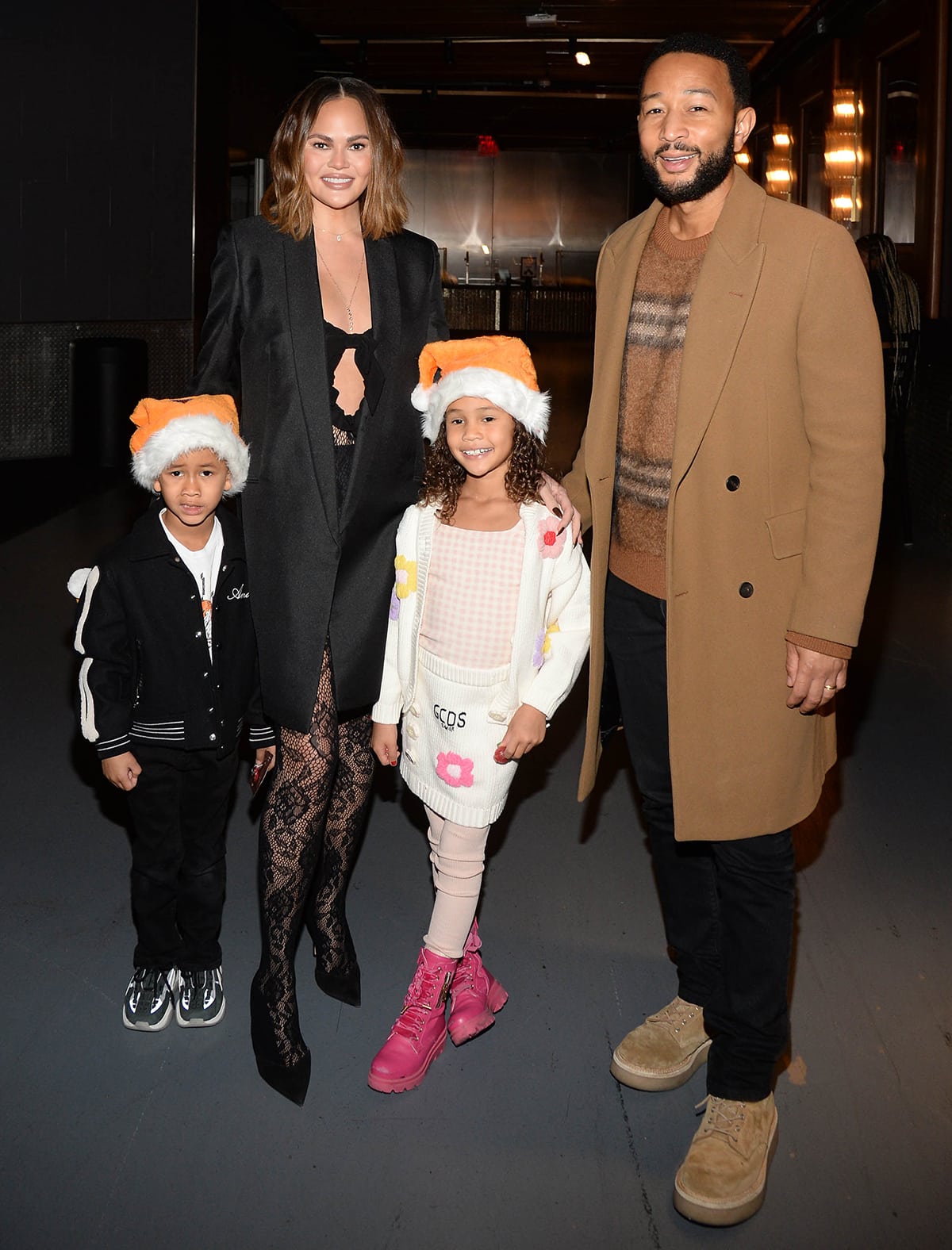 Chrissy Teigen opts for a sultry outfit consisting of a black lace cutout bra, see-through floral lace leggings, and a black coat for the basketball game