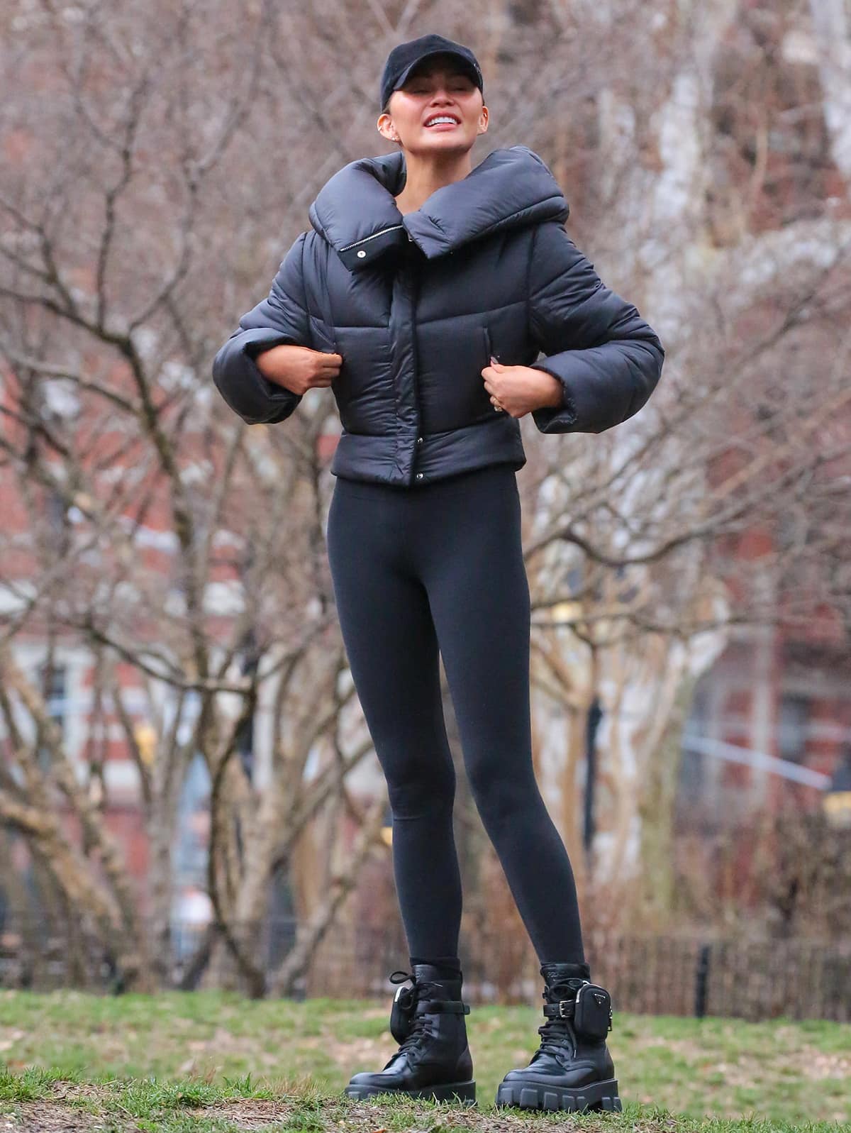 Chrissy Teigen plays football and flies drones with her kids and husband John Legend in comfy black leggings, a bra top, and a black puffer jacket at Washington Square Park on December 28, 2023