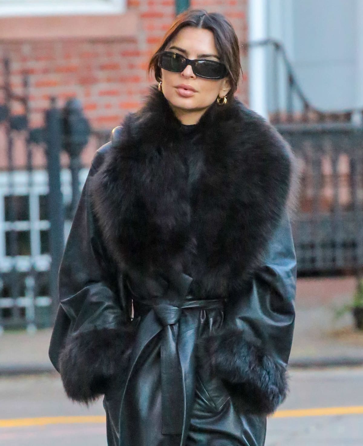 Emily Ratajkowski adds glitz to her all-black winter outfit with thick gold hoops and shields her eyes with Dolce Gabbana Edition sunnies