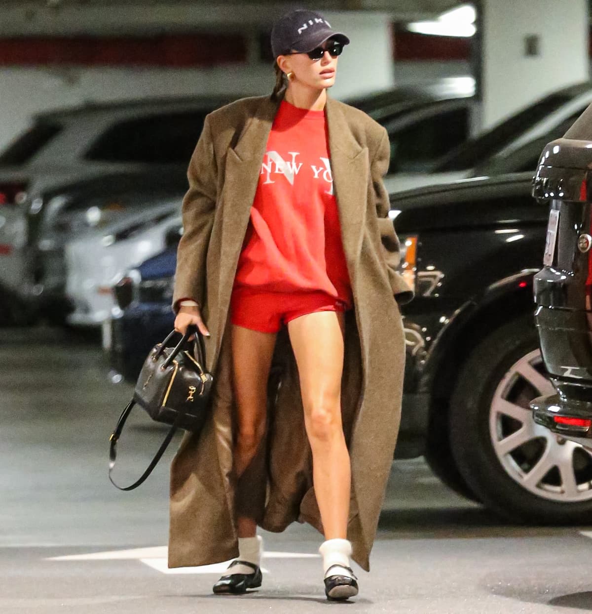 Hailey Bieber shines with minimalist makeup, a neatly styled braid, gold hoop earrings, and a chic Saint Laurent duffle bag
