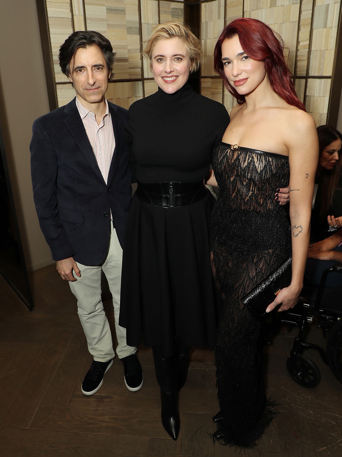 Dua Lipa stuns in a strapless black Gucci naked dress with beaded fringe while posing alongside “Barbie” director Greta Gerwig, who opted for a belted black turtleneck dress and knee-high boots, and filmmaker Noah Baumbach in a smart blazer and sneakers
