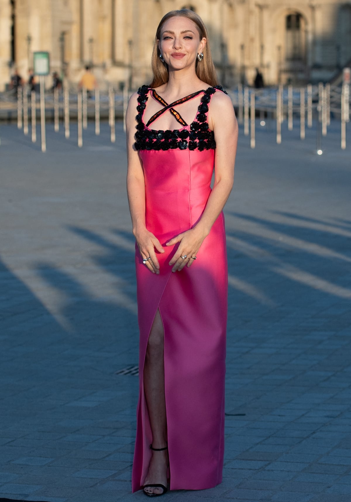Amanda Seyfried dazzles in a custom Barbie pink Prada gown at the Lancôme x Louvre photocall during Paris Fashion Week, embodying vibrant, modern elegance with sleek black sandals completing the look
