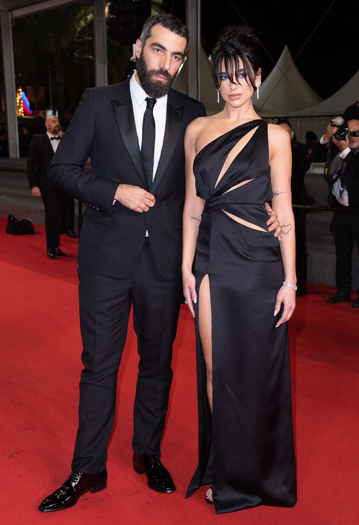 Romain Gavras and Dua Lipa attend the “Omar La Fraise” premiere at the 76th Cannes Film Festival on May 19, 2023, with Gavras in a classic tuxedo and Dua in a daring black cutout gown paired with strappy red heeled sandals