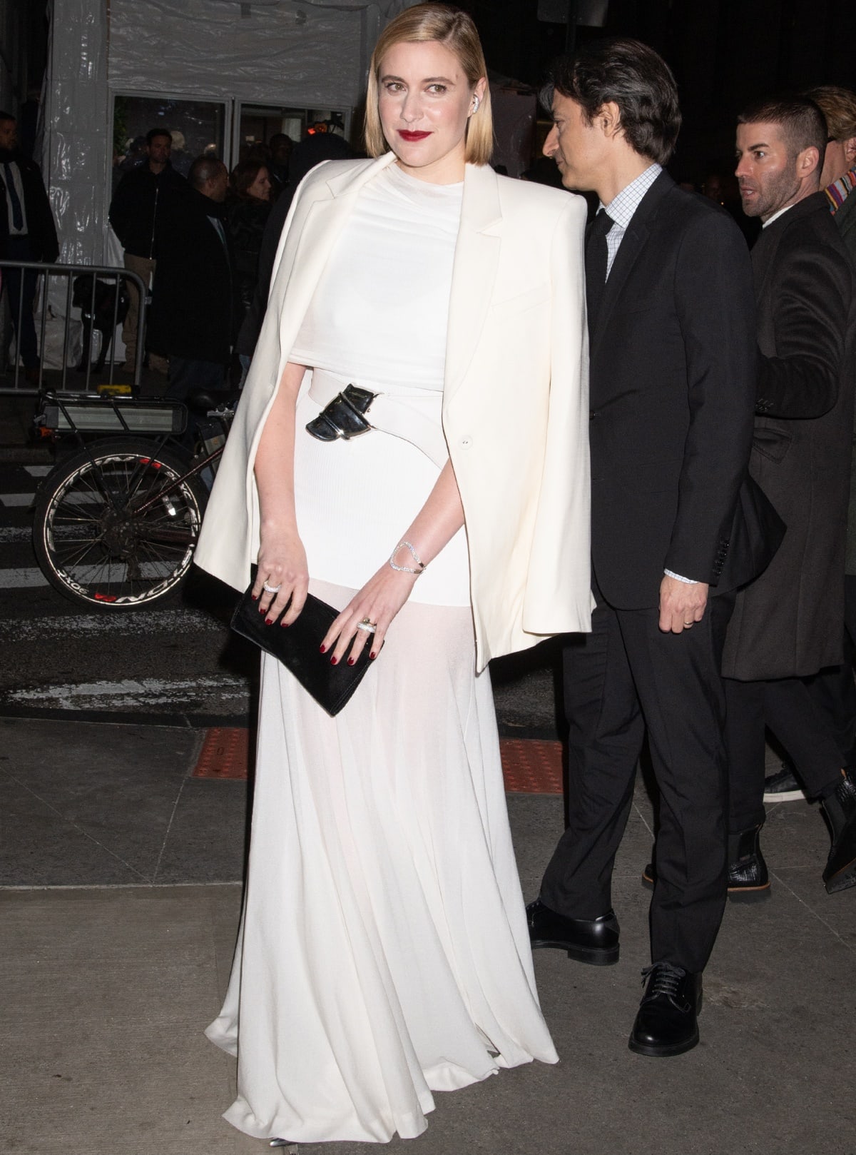 Greta Gerwig radiated minimalist glamour in a white Brandon Maxwell ensemble—complete with a cape blazer and statement belt—while keeping her heels hidden beneath the floor-grazing hem