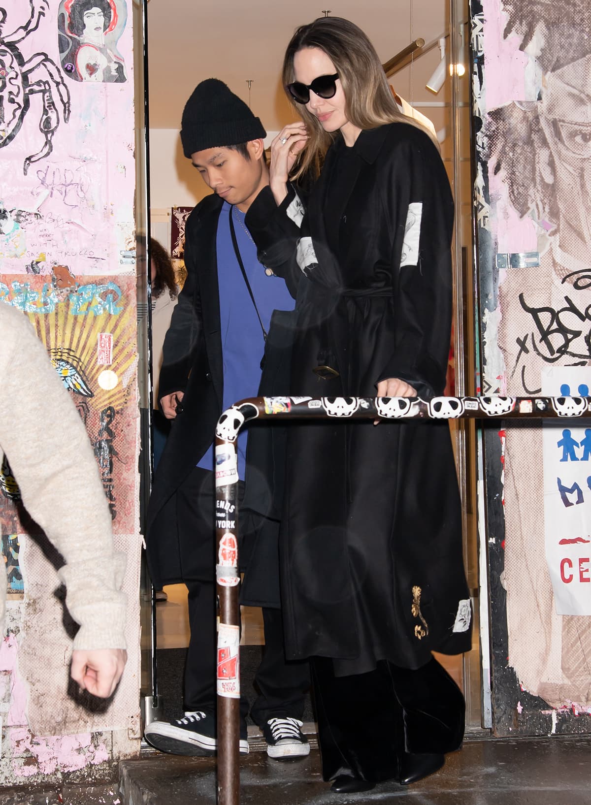 Angelina Jolie steps out of Atelier Jolie in Greenwich Village wearing a black embroidered trench coat, velvet wide-leg trousers, and sharp pointed-toe leather boots while son Pax keeps things casual in Converse sneakers and layered winter basics on December 28, 2023