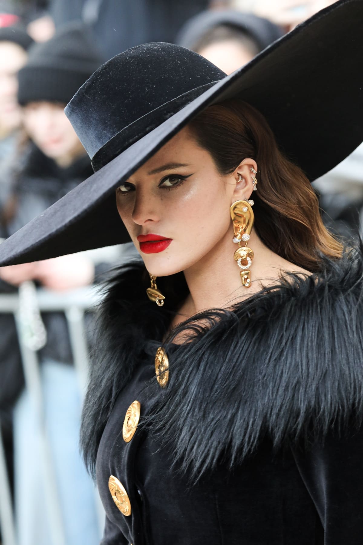 Bella Thorne commands attention in an off-shoulder Schiaparelli pantsuit, pairing it with Anatomy Bijoux earrings and a sleek black hat at the Schiaparelli show