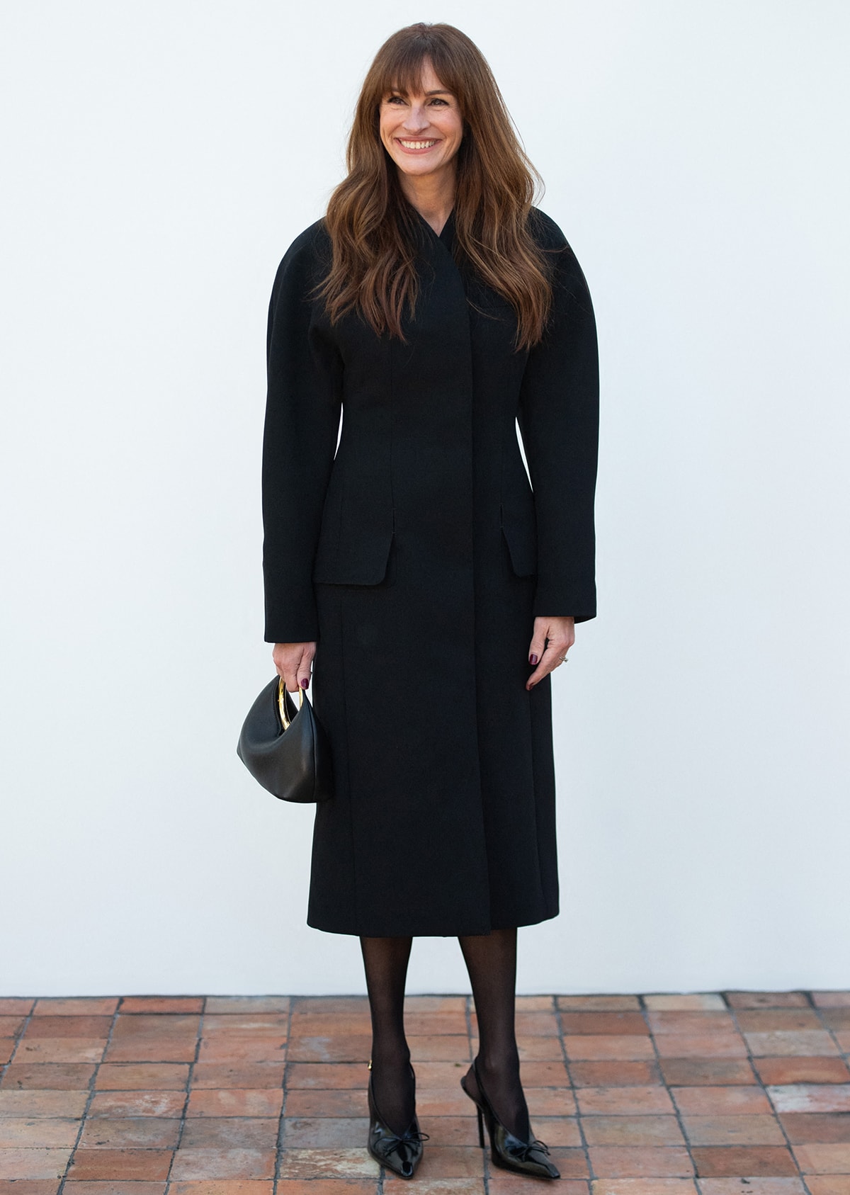 Opting for a regal look, Julia Roberts embraces quiet luxury in a structured black Jacquemus coat dress, sheer tights, and Jacquemus Les Slingbacks Cubito Hautes shoes