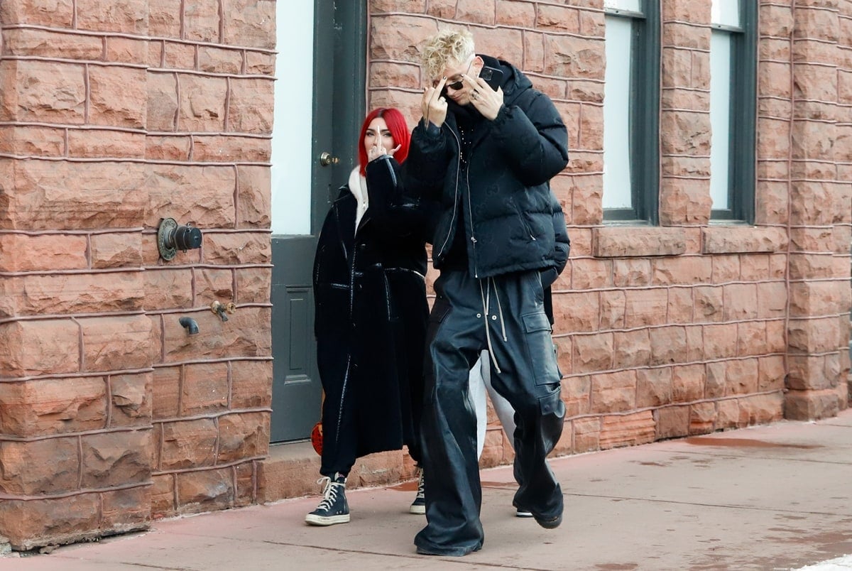 Megan Fox and MGK bring edgy winter street style to Aspen on December 31, 2023, with Fox pairing a long black coat and red hair with classic lace-up sneakers while MGK layers a puffer jacket over baggy cargo pants for a monochrome, off-duty finish