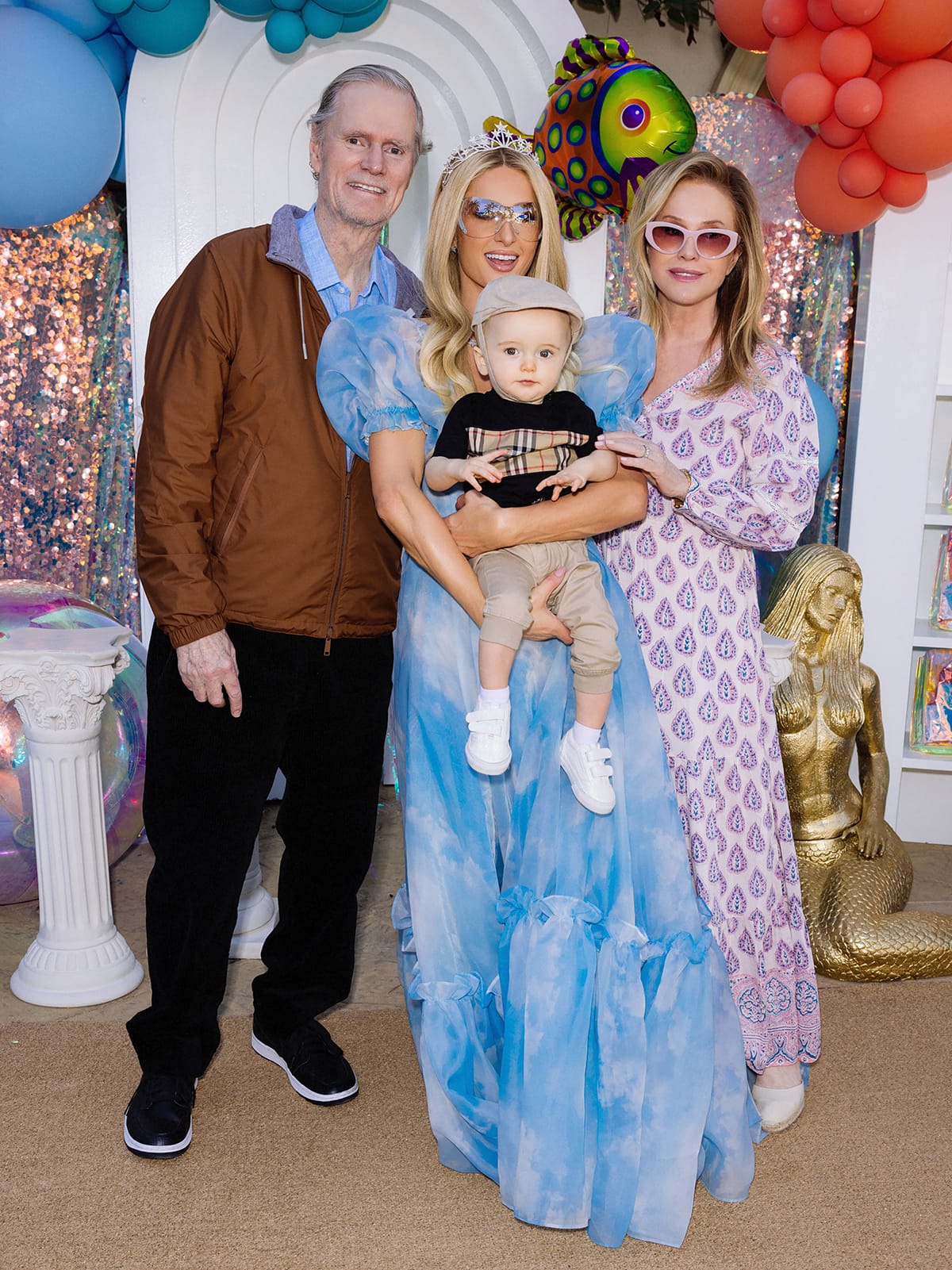 Paris Hilton, dressed in her cloud-printed Selkie gown, poses with her son Phoenix and her parents Rick and Kathy Hilton during the whimsical “Sliving Under the Sea” birthday celebration