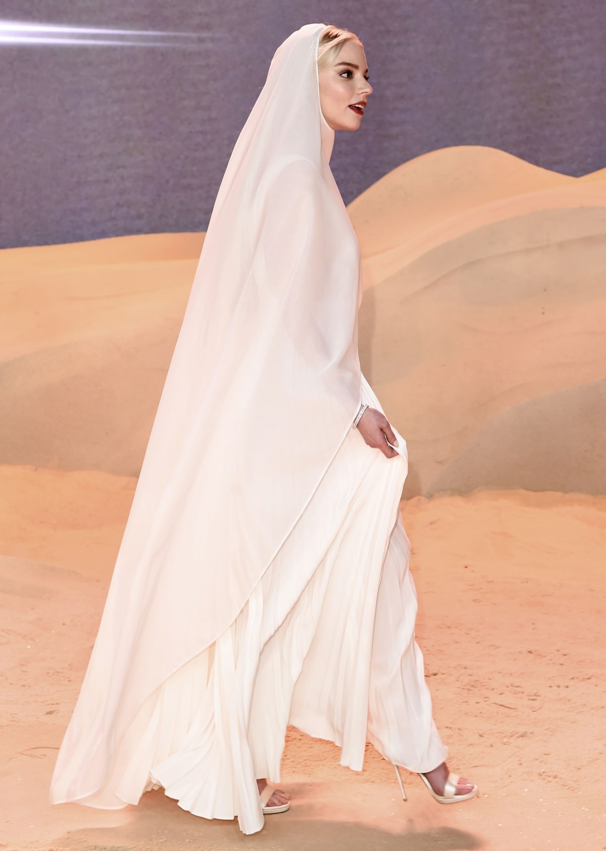 Anya Taylor-Joy glides across the Dune-inspired red carpet in a vintage-inspired Dior Haute Couture gown layered with a sheer hooded cape and paired with minimalist white stiletto sandals