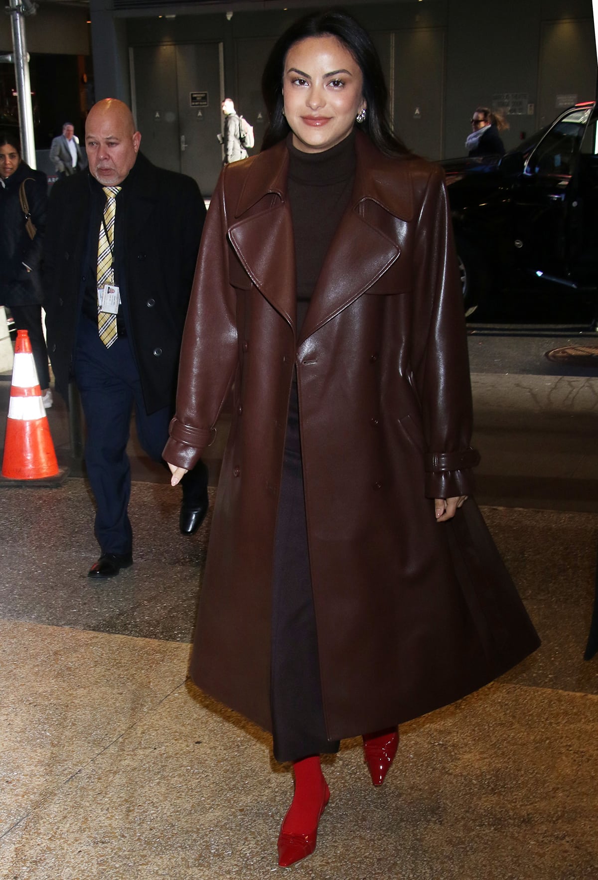 Camila Mendes drops by CBS Mornings in a toffee Alice + Olivia leather trench coat layered over a cocoa Sandy Liang sweater and midi skirt combo on February 6, 2024