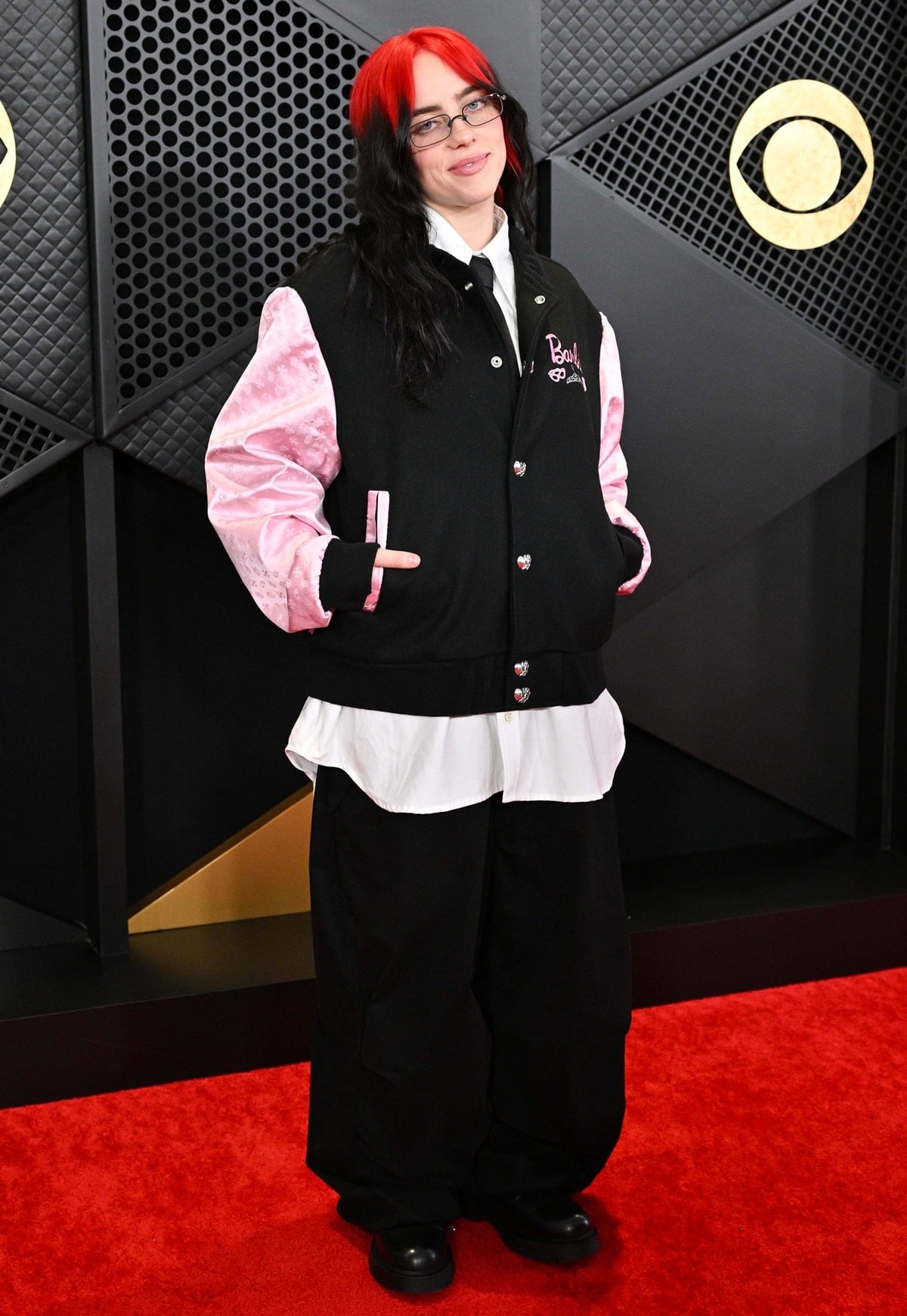 Petite singer Billie Eilish attended the 2024 Grammy Awards in a vintage Barbie-themed Chrome Hearts bomber jacket, rocking pink sleeves and "Barbie" embroidery with a casual white button-down and black pants