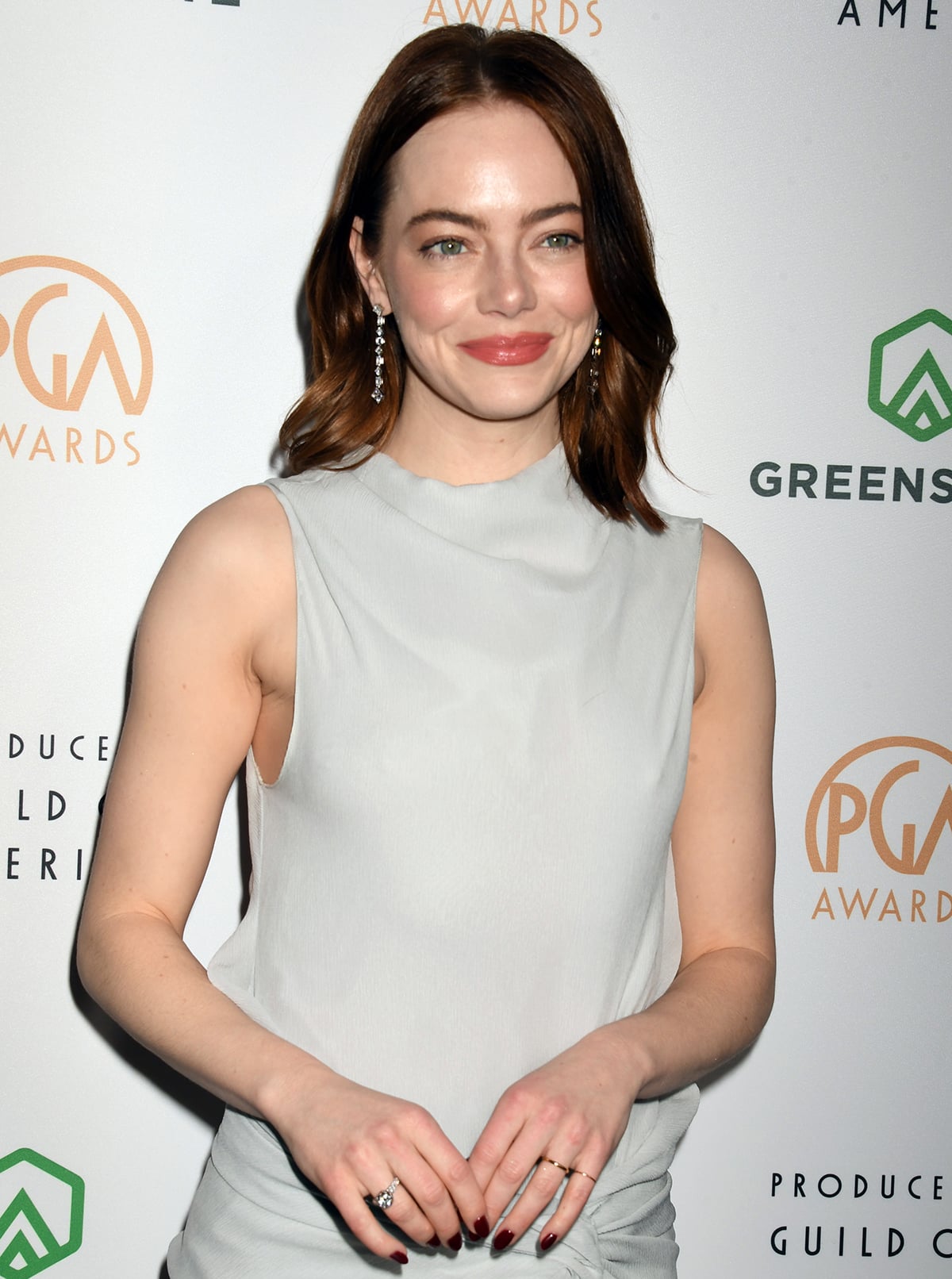 Emma Stone styles her muted gray look with sparkling dangling diamonds on her ears and a few rings on her manicured hands, all by Tiffany Co.