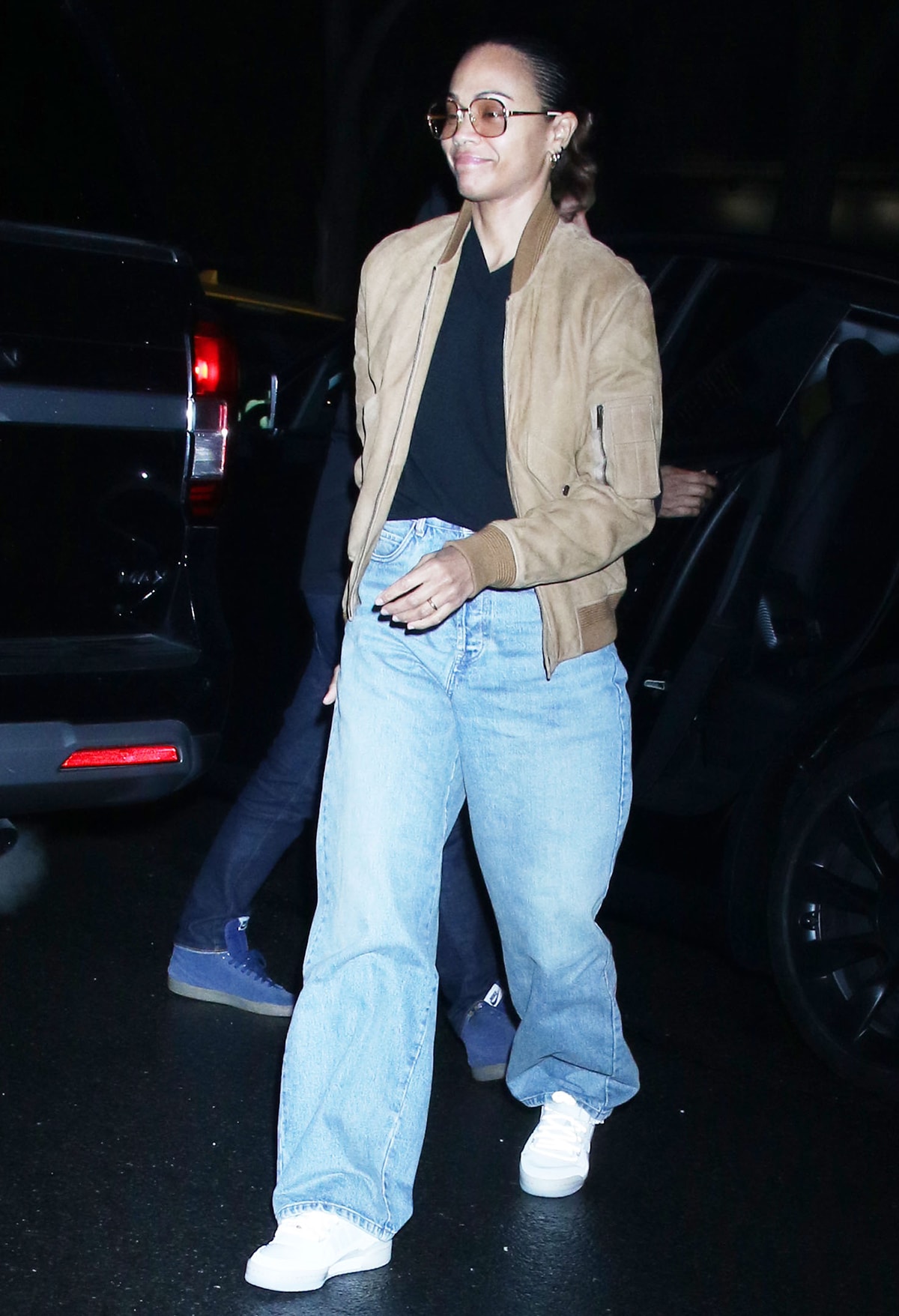 Zoe Saldaña dresses casually in a black tee, baggy jeans, white sneakers, and a camel bomber jacket as she arrives at her Greenwich hotel on March 27, 2024