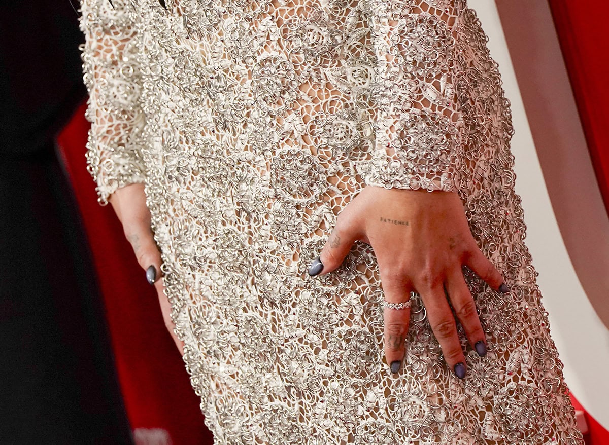 Dua Lipa's hand, tattooed with 'PATIENCE' and adorned with Tiffany Co. rings, adds a touch of sparkle to her luxurious ensemble