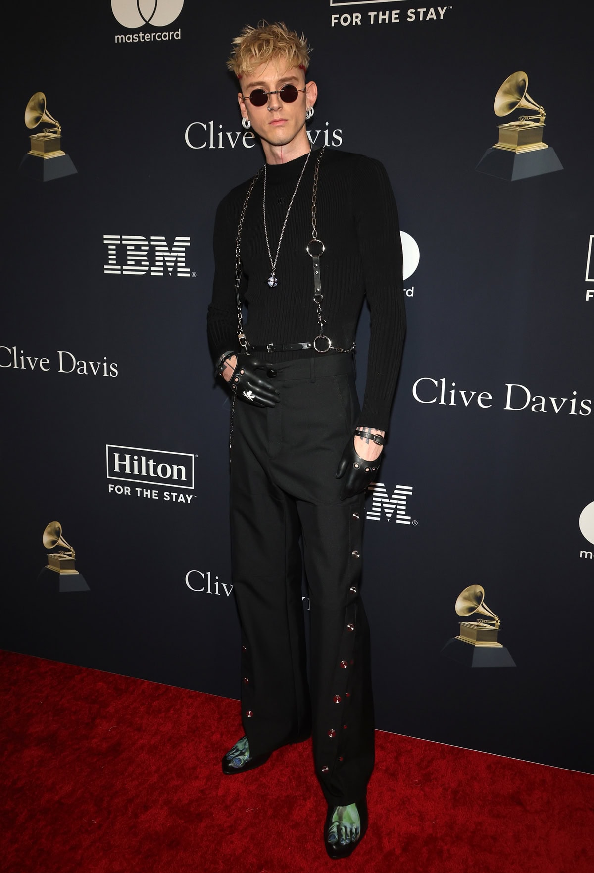 Machine Gun Kelly embraces edgy fashion in a black harnessed outfit and eye-catching green toe-printed shoes at the Clive Davis Pre-Grammy Gala
