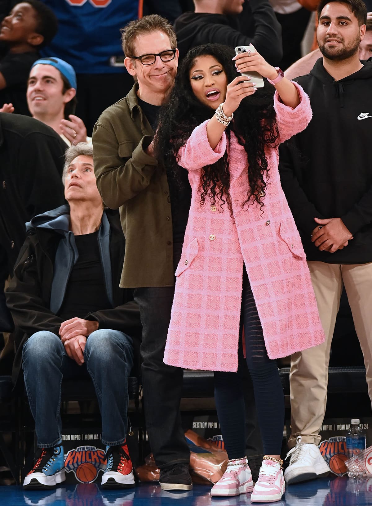 Nicki Minaj poses for a courtside selfie with Ben Stiller while attending the New York Knicks vs. Oklahoma City Thunder game at Madison Square Garden on March 31, 2024, wearing a pink Chanel tweed coat, sheer Alaïa striped leggings, and pink-and-white Loci “Atom” sneakers