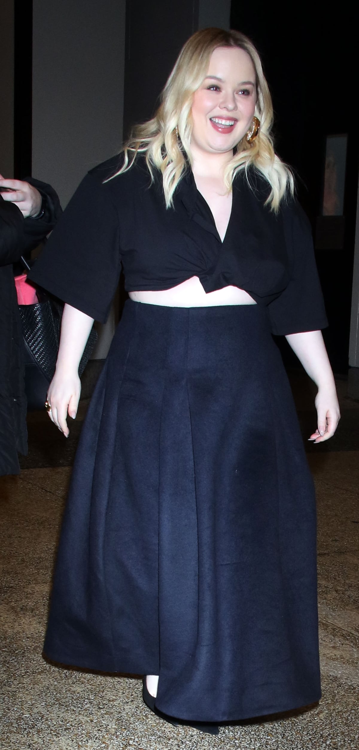 Nicola Coughlan exuded elegance in a black crop top with pleated detailing and a plunging neckline, paired with a chic maxi skirt and pointed heels for a CBS studio appearance in NYC, complemented by loose wavy hair and gold earrings