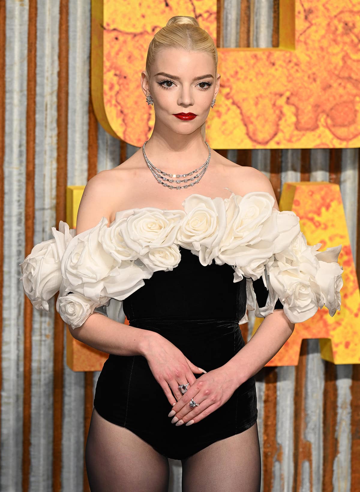Anya Taylor-Joy styles her off-the-shoulder bodysuit with Tiffany Co. jewelry, including a three-strand necklace, and wears vibrant red lipstick for a pop of color