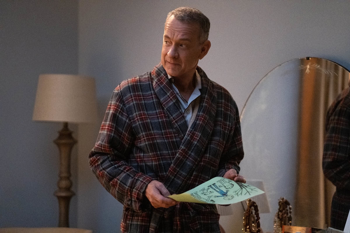 Tom Hanks embodies the role of Otto Anderson, offering a reflective glance while holding a child's artwork, dressed comfortably in a tartan robe—capturing a quiet, reflective moment in A Man Called Otto
