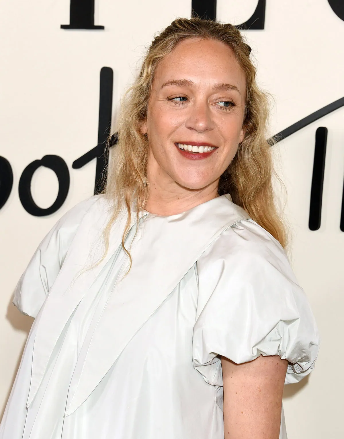 Chloë Sevigny adds a coquette element to her whimsical look by styling her long curly tresses with a black bow
