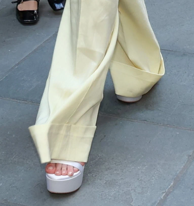 Dakota Fanning completes her yellow co-ords with white satin Stuart Weitzman “Nudist Hollywood” platform sandals featuring slender straps and towering heels