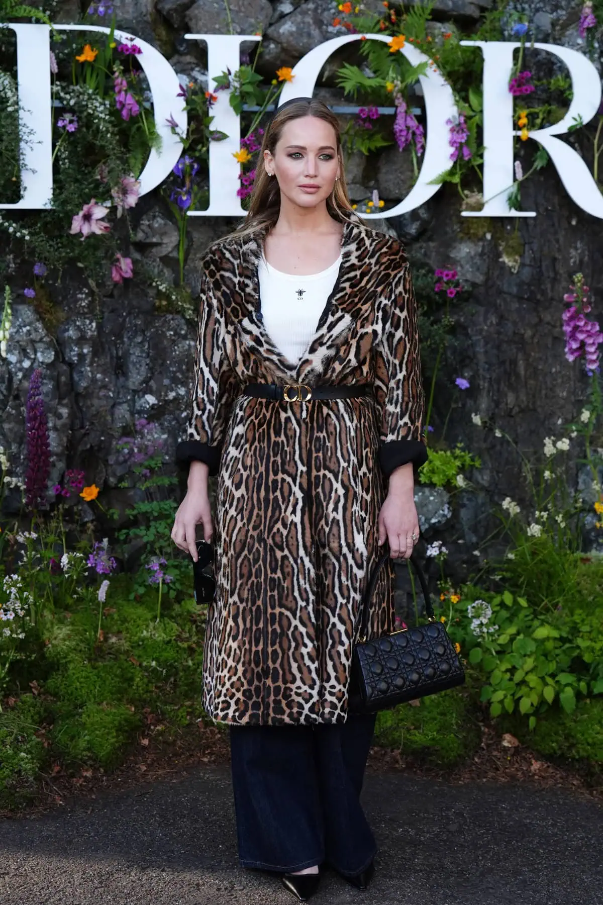 Jennifer Lawrence stunning in a white ribbed Dior tank top and high-waisted denim jeans, embodying understated luxury at Dior's Cruise 2025 collection show
