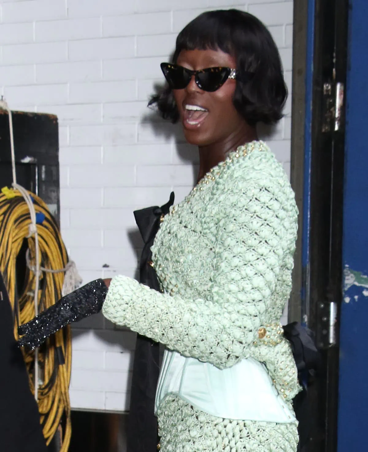 Jodie Turner-Smith teams her green crocheted outfit with the Bottega Veneta cat-eye shades, black gloves, and retro hairstyle